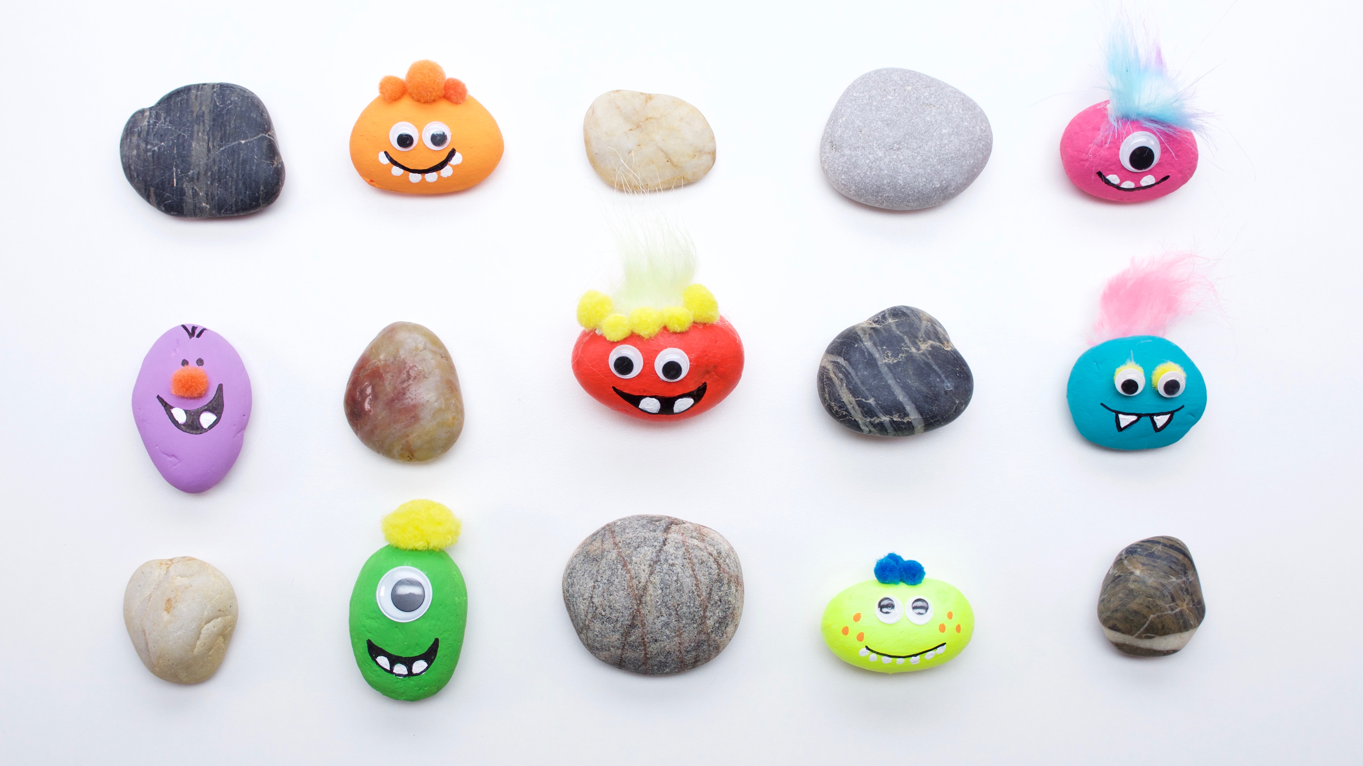 Several small stones painted in different colors, with funny faces on them, sit in rows against a white background.
