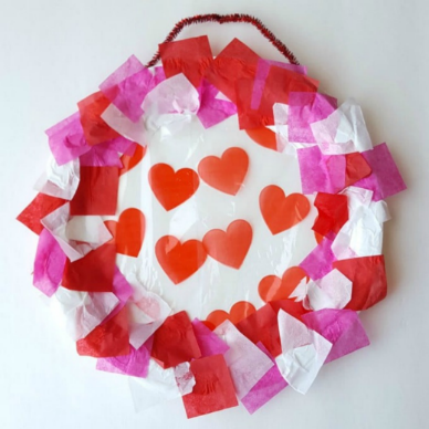 Paper plate wreath with white, pink, and red tissue paper hearts stuck on the sides and in the middle.