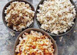 Three bowls of caramel, plain, and cheese popcorn sit on a gray marble table.