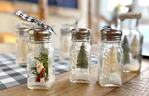 A group of salt shakers sits on a wooden table with pine tree figurines inside each one. 