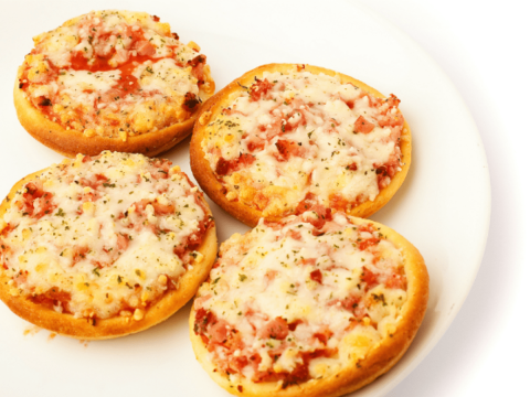 Four mini pizzas made out of English muffins, tomato sauce, and melted mozzarella cheese sit on a white plate.