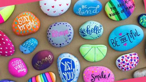 Small painted rocks with kind messages sit on top of a brown background.