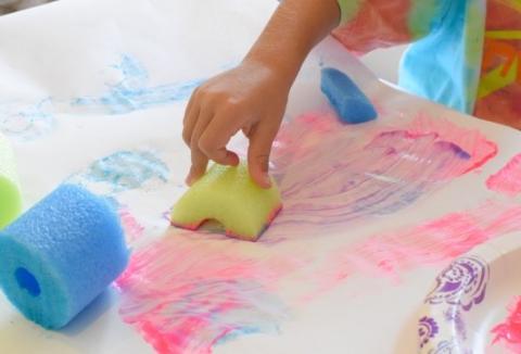 A person paints a pink squiggle with a piece of a green pool noodle.