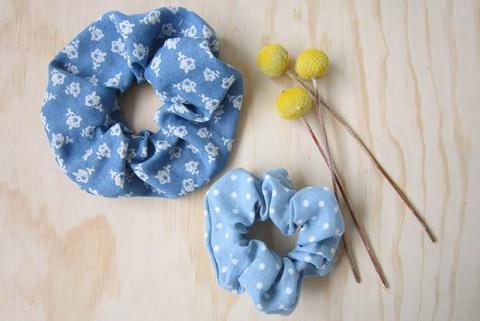 Two blue DIY scrunchies sit next to several knitting needles.