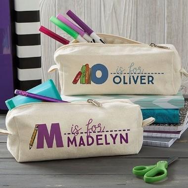 Two pencil cases, personalized with the names Madelyn and Oliver, sit beside a pile of other school supplies.