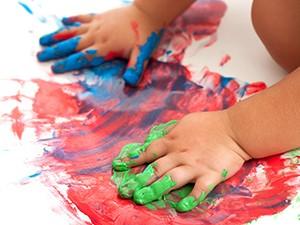 A toddler uses their hands to paint on a piece of white paper.