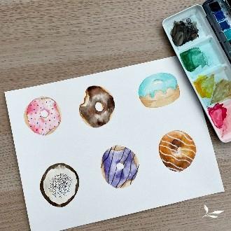 Photo of several small donuts painted with watercolors on a white piece of paper. A tray of open watercolors sits next to it.
