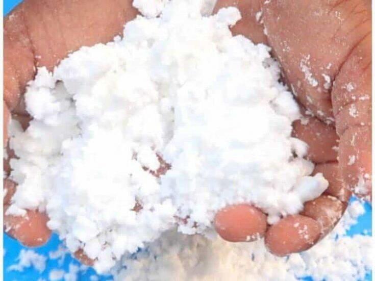 A light-skinned person holds powdery white fake snow in their hands.