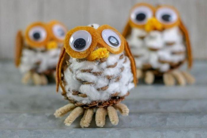 Three small owls made out of pinecones, felt, and pipe cleaners sit on a gray surface.