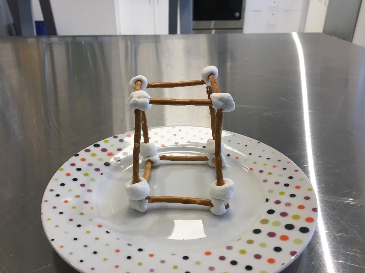 A structure made of marshmallows and small pretzel sticks sits on a plate.