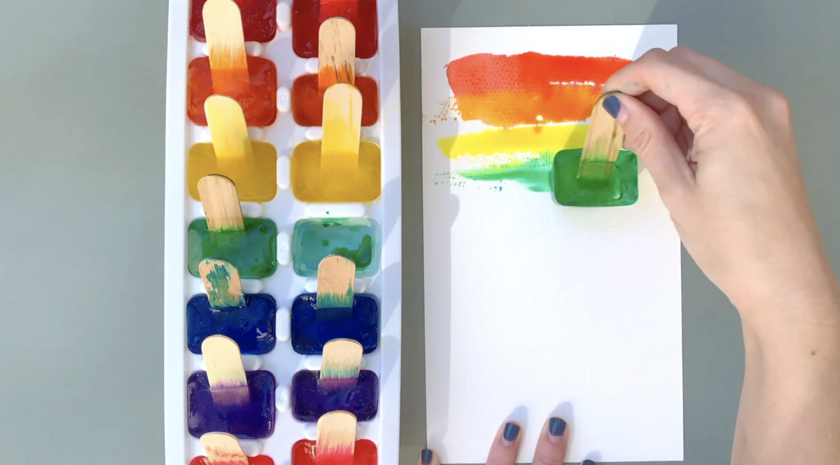 A light skinned hand paints multicolored lines using an ice cube.